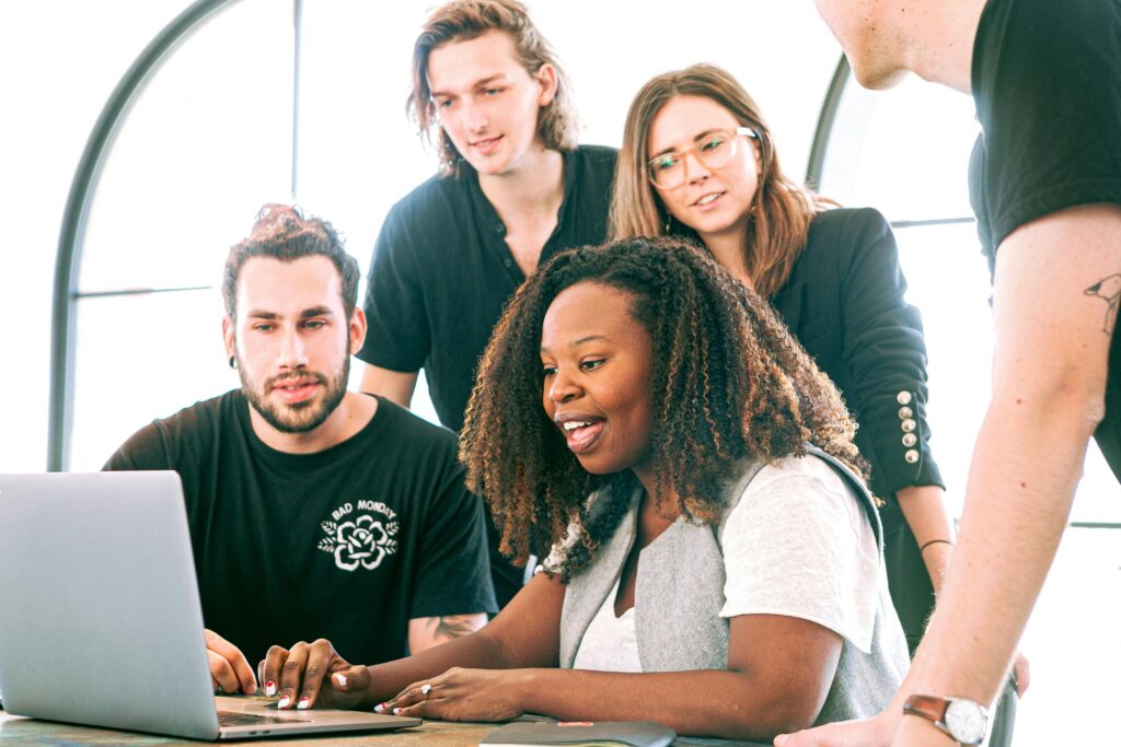 A diverse group of young professionals collaborating around a laptop in a modern office setting. Perfect for business or tech concepts.