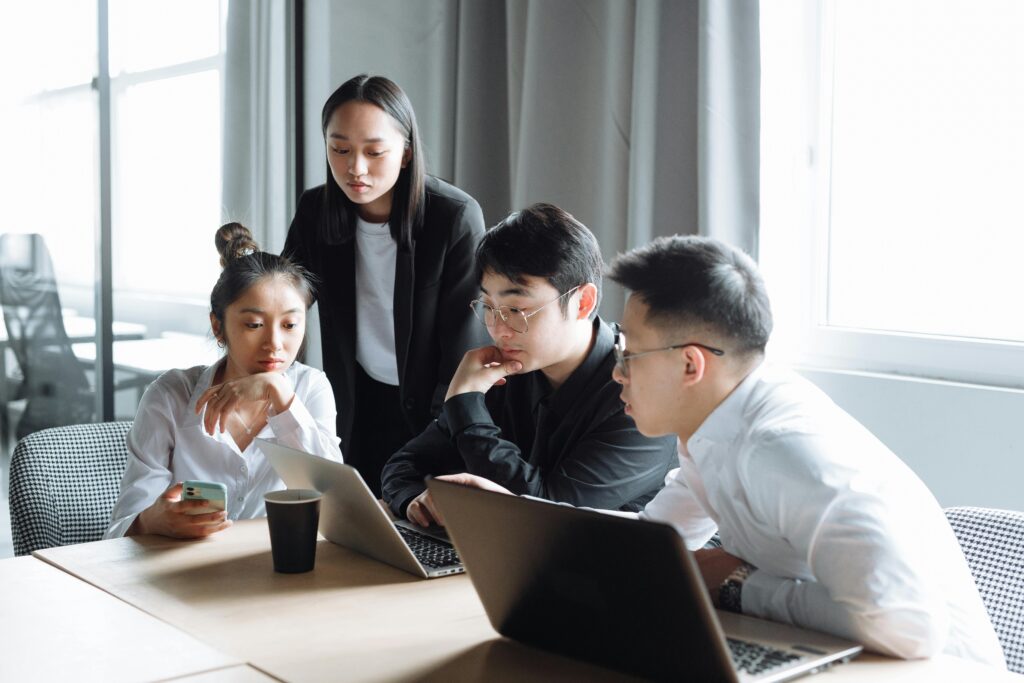 A group of Asian professionals engaged in a collaborative business meeting in a bright office setting.